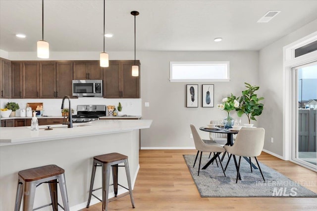 kitchen with a breakfast bar, hanging light fixtures, stainless steel appliances, dark brown cabinets, and light wood-type flooring