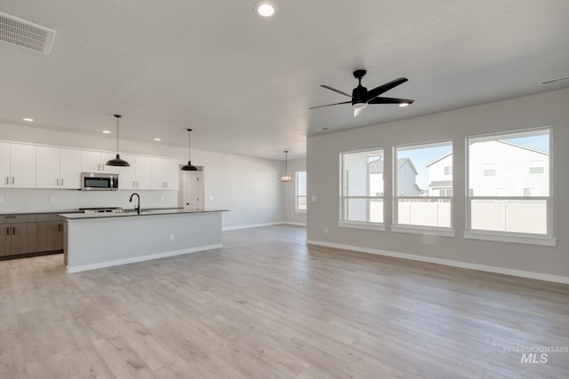 kitchen featuring visible vents, open floor plan, light wood finished floors, tasteful backsplash, and stainless steel microwave