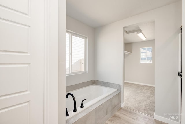 bathroom featuring wood finished floors, a garden tub, and baseboards