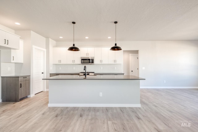 kitchen with light wood-type flooring, stainless steel microwave, stove, and a center island with sink