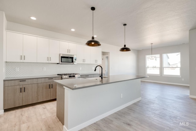 kitchen featuring appliances with stainless steel finishes, a kitchen island with sink, a sink, and backsplash