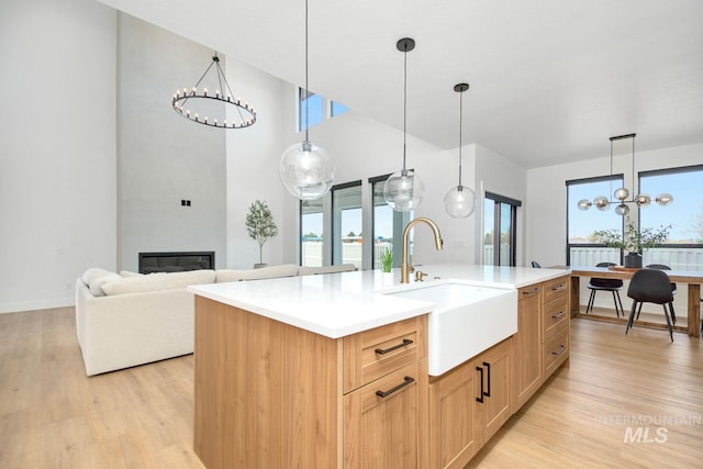 kitchen with pendant lighting, light brown cabinets, a center island with sink, sink, and a fireplace