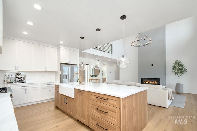 kitchen featuring stainless steel refrigerator with ice dispenser, a kitchen island with sink, light hardwood / wood-style flooring, white cabinets, and hanging light fixtures