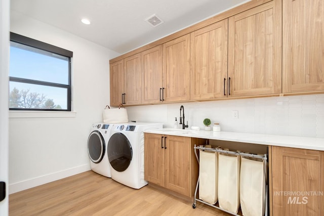 clothes washing area featuring washer and clothes dryer, sink, cabinets, and light hardwood / wood-style flooring