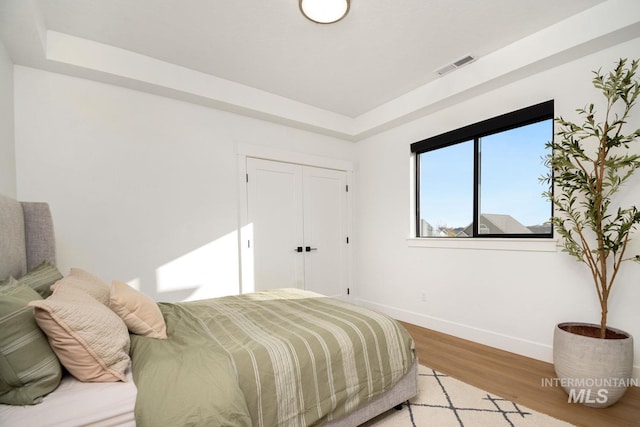 bedroom with a raised ceiling, light wood-type flooring, and a closet