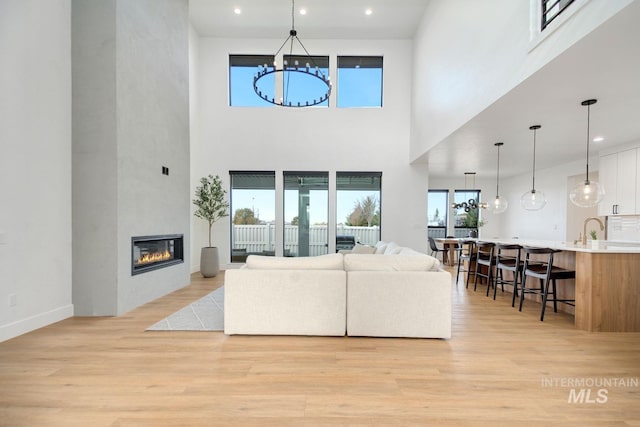 living room featuring sink, a fireplace, a high ceiling, and light hardwood / wood-style flooring