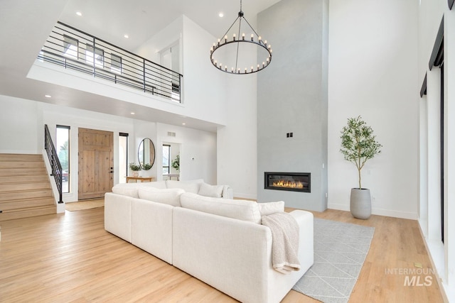 living room with a high ceiling, an inviting chandelier, and light hardwood / wood-style flooring