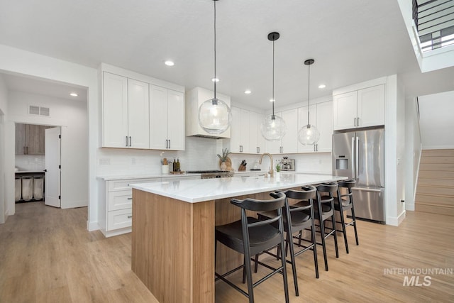 kitchen with white cabinetry, light hardwood / wood-style flooring, an island with sink, and stainless steel refrigerator with ice dispenser