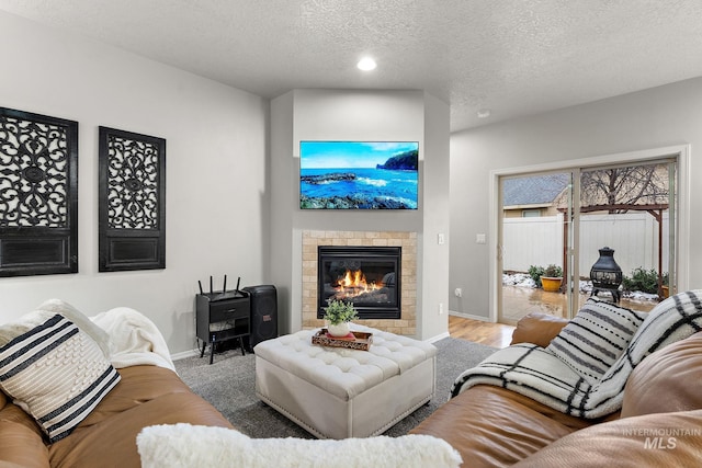 living room with baseboards, a tiled fireplace, wood finished floors, a textured ceiling, and recessed lighting