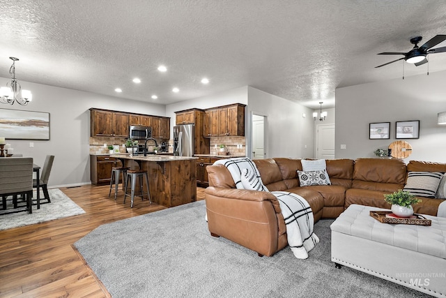 living room with light wood finished floors, ceiling fan with notable chandelier, a textured ceiling, and recessed lighting