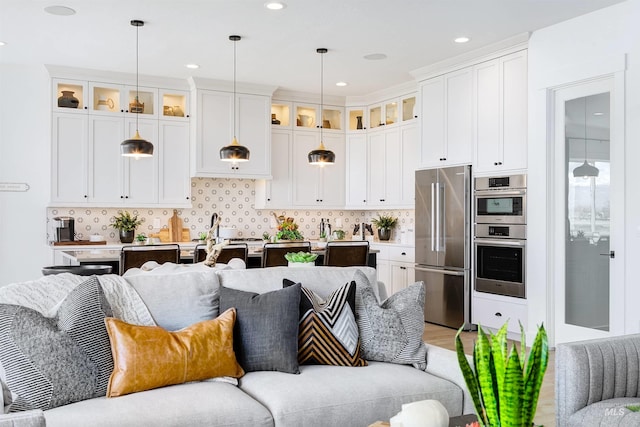 kitchen featuring stainless steel appliances, open floor plan, glass insert cabinets, decorative light fixtures, and recessed lighting