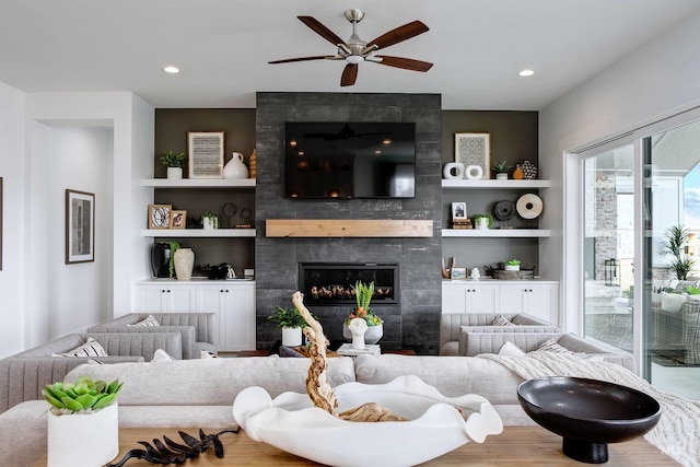 living room featuring a tiled fireplace, a ceiling fan, built in features, recessed lighting, and wood finished floors
