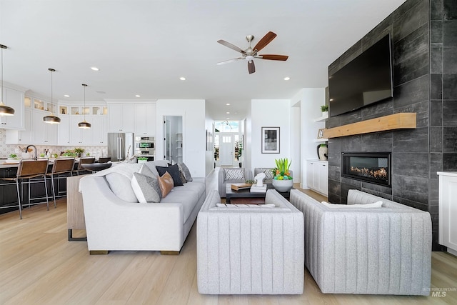 living room with a ceiling fan, light wood finished floors, a tile fireplace, and recessed lighting