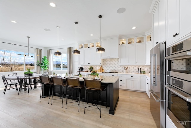 kitchen with stainless steel appliances, light countertops, backsplash, light wood-style floors, and a breakfast bar