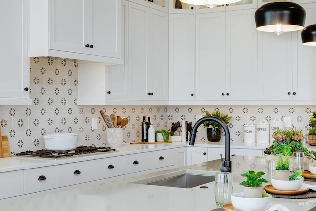 kitchen featuring white cabinets, light countertops, tasteful backsplash, a sink, and glass insert cabinets