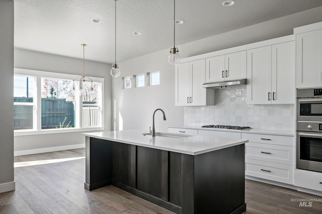 kitchen with stainless steel double oven, under cabinet range hood, a sink, gas stovetop, and light countertops