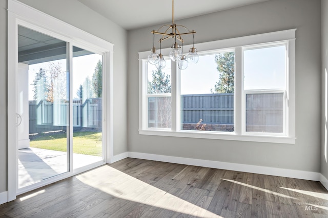 unfurnished dining area featuring a notable chandelier, wood finished floors, and baseboards