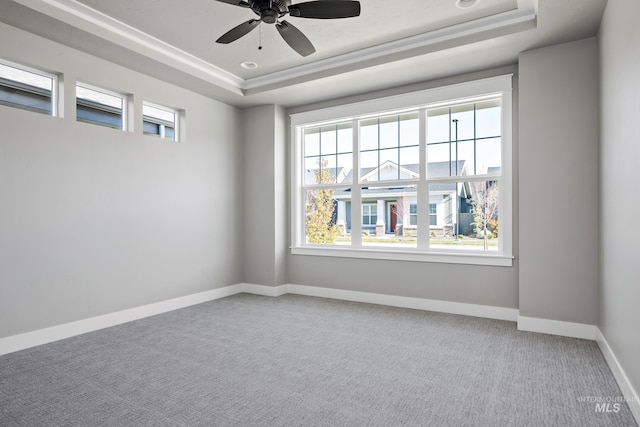 carpeted empty room with a raised ceiling, a ceiling fan, and baseboards