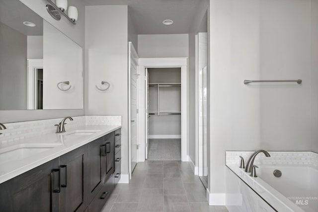 full bath featuring double vanity, a garden tub, tile patterned flooring, a walk in closet, and a sink