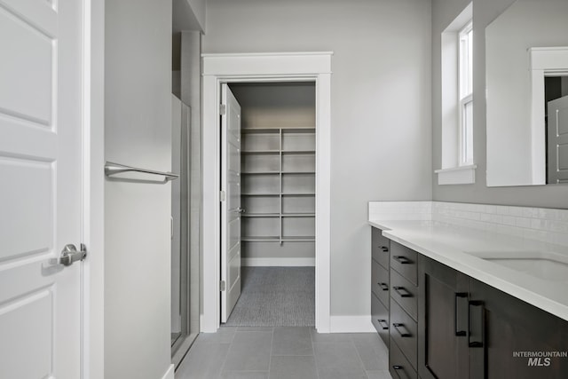 full bathroom with a stall shower, baseboards, tile patterned flooring, a spacious closet, and vanity