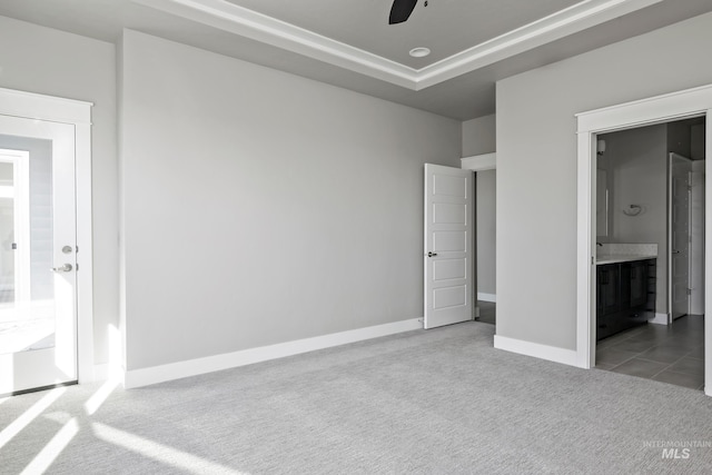 unfurnished bedroom featuring carpet, a raised ceiling, ceiling fan, ensuite bath, and baseboards