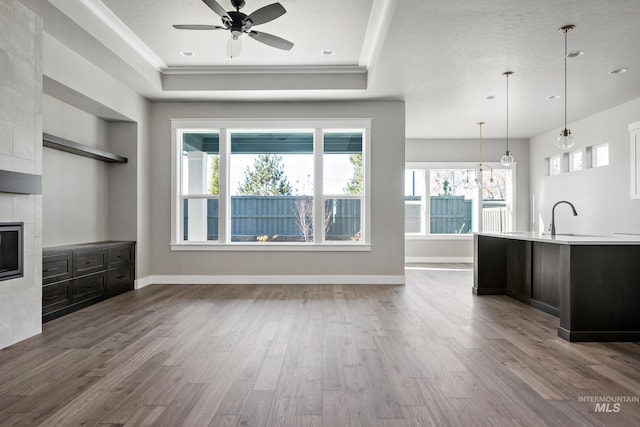 unfurnished living room featuring ceiling fan, a raised ceiling, dark wood finished floors, and baseboards