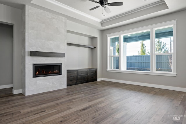 unfurnished living room featuring a fireplace, wood finished floors, baseboards, a tray ceiling, and crown molding