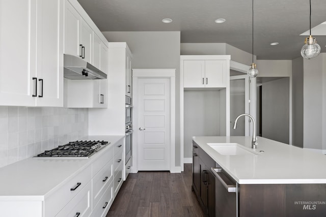 kitchen featuring dark wood finished floors, stainless steel appliances, light countertops, under cabinet range hood, and a sink