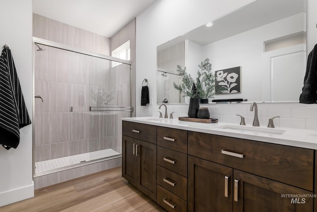 full bathroom featuring a sink, tiled shower, wood finished floors, and double vanity