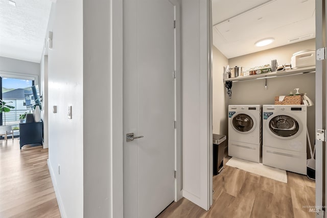 laundry area featuring a textured ceiling, light wood finished floors, baseboards, laundry area, and washing machine and clothes dryer