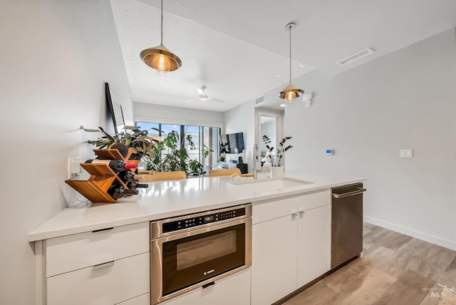 kitchen featuring visible vents, a sink, white cabinets, pendant lighting, and stainless steel oven