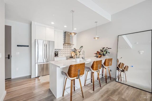 kitchen featuring backsplash, wall chimney range hood, a breakfast bar, stainless steel appliances, and white cabinetry