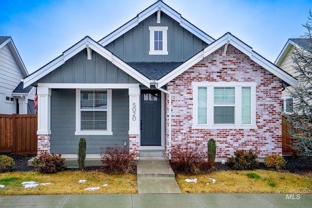 view of front of home featuring a shingled roof, fence, board and batten siding, and brick siding