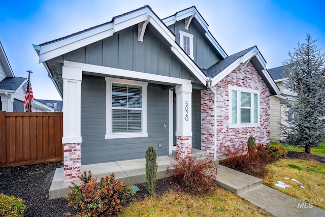 view of front of property with brick siding, board and batten siding, a porch, and fence