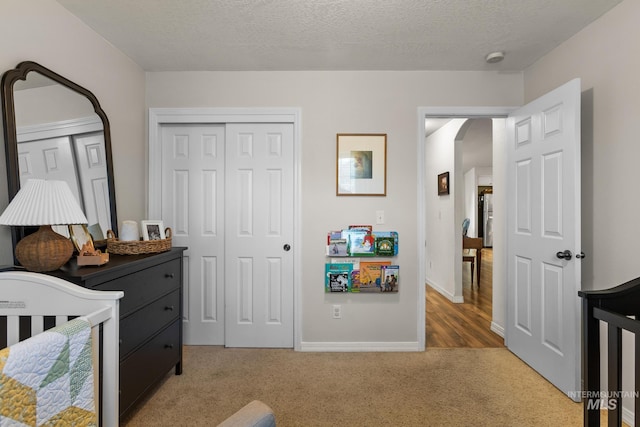 carpeted bedroom with a textured ceiling, a closet, and a nursery area