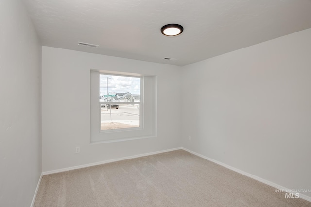 spare room with light colored carpet, visible vents, and baseboards