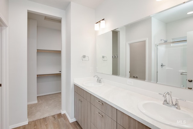 bathroom with a walk in closet, a shower with door, a sink, and double vanity