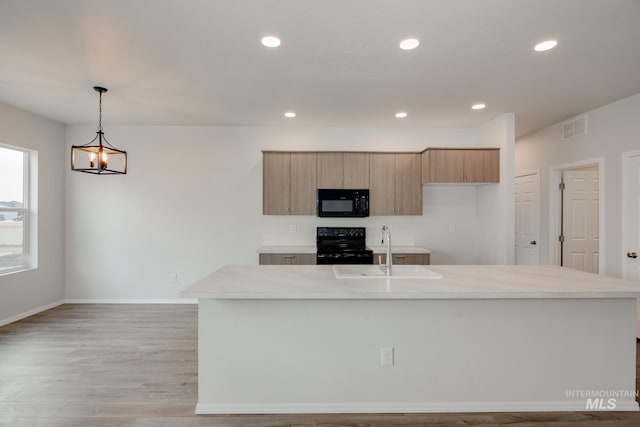 kitchen featuring light countertops, hanging light fixtures, a kitchen island with sink, a sink, and black appliances