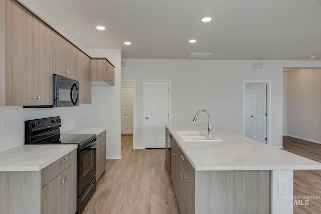 kitchen featuring visible vents, light countertops, a sink, an island with sink, and black appliances