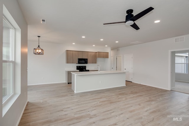 kitchen featuring hanging light fixtures, black appliances, light countertops, and an island with sink