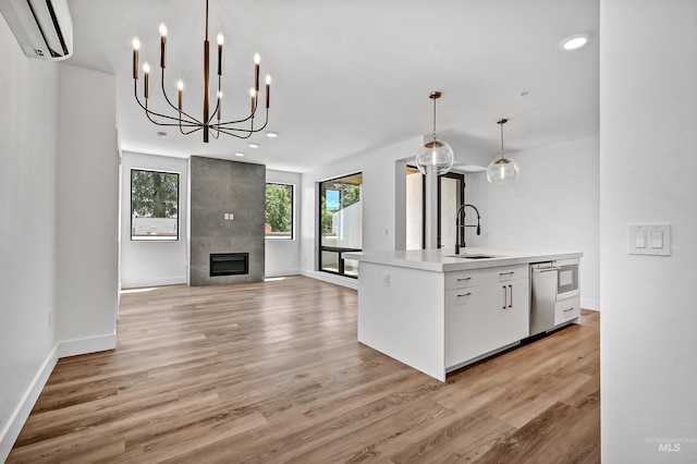 kitchen featuring hanging light fixtures, light hardwood / wood-style flooring, a wall mounted AC, a fireplace, and white cabinets