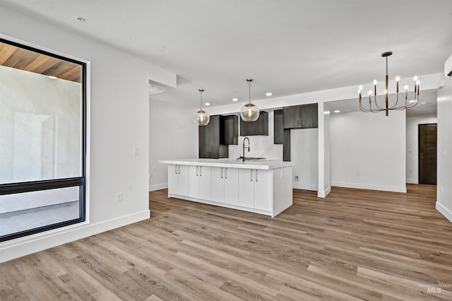 kitchen featuring a kitchen island with sink, sink, decorative light fixtures, light hardwood / wood-style flooring, and a chandelier