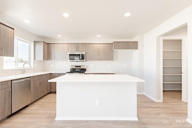 kitchen featuring appliances with stainless steel finishes, a center island, decorative backsplash, and light wood-type flooring