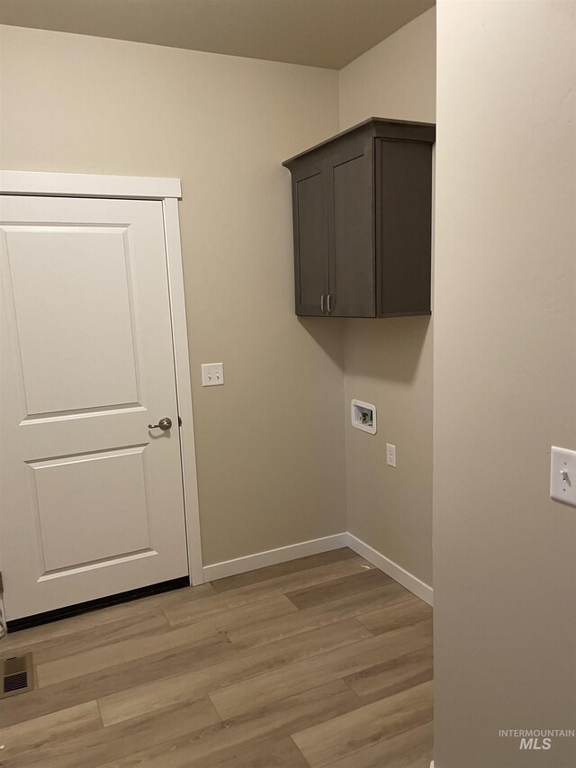 clothes washing area featuring visible vents, baseboards, cabinet space, washer hookup, and light wood-style floors
