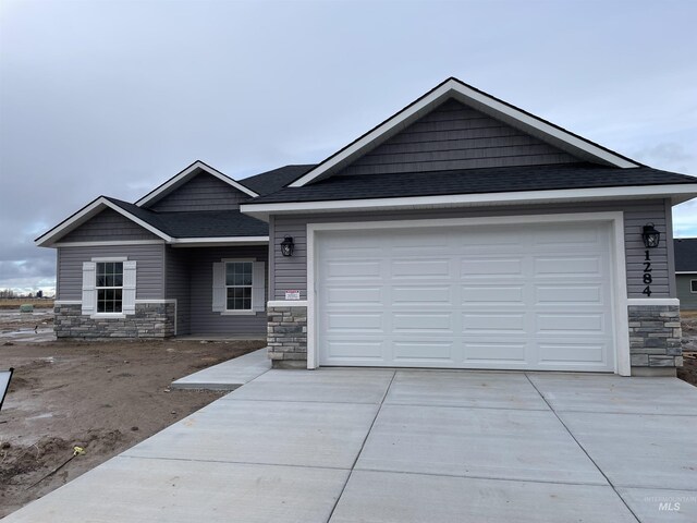 view of front of property with stone siding, driveway, a garage, and roof with shingles