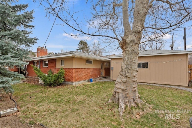 back of house with a yard, a chimney, and brick siding