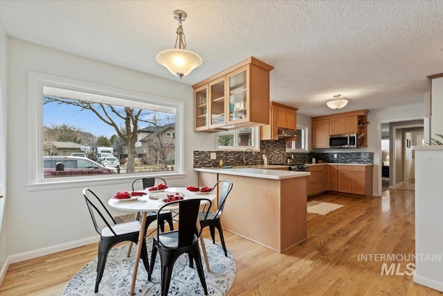 kitchen featuring decorative backsplash, stainless steel microwave, glass insert cabinets, a peninsula, and light wood-style floors