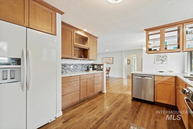 kitchen with light wood finished floors, white refrigerator with ice dispenser, dishwasher, light countertops, and backsplash