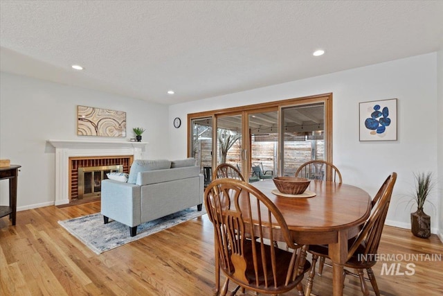 dining room featuring a textured ceiling, light wood finished floors, a brick fireplace, and baseboards