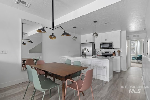 dining space with sink, a textured ceiling, and light wood-type flooring